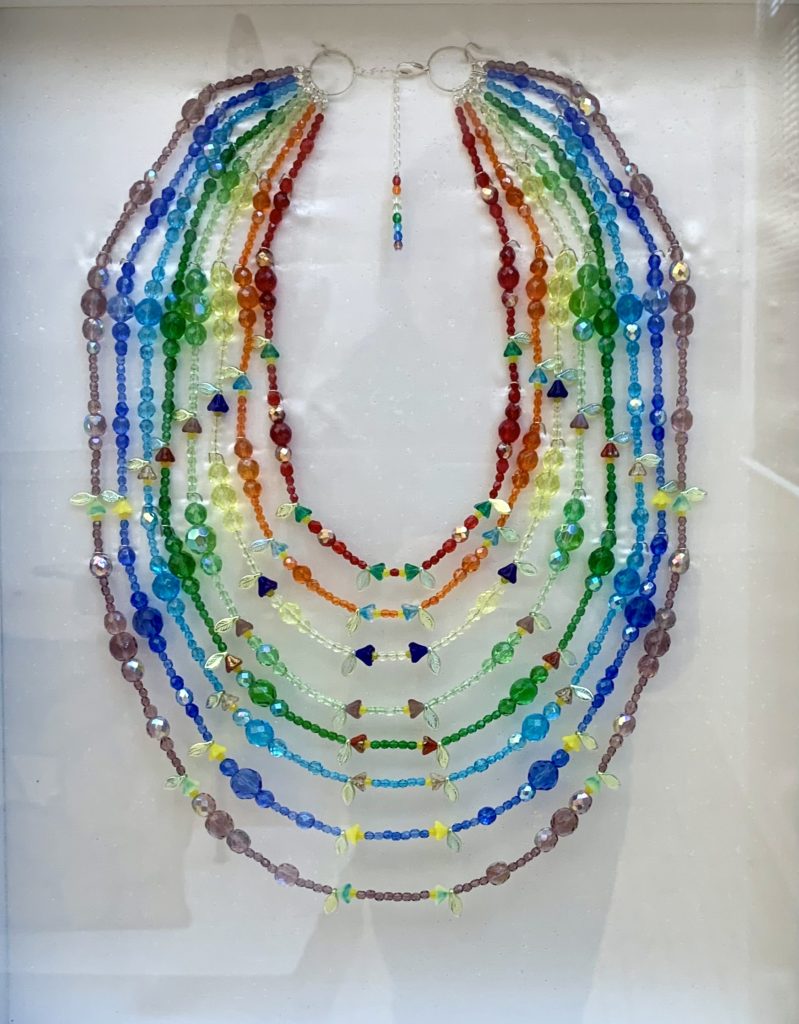 "moquiej" - a necklace for Arts Center East Member Exhibit. It has eight strands with each strand a different color of the rainbow. Each strand also has flowers made with Czech glass beads.